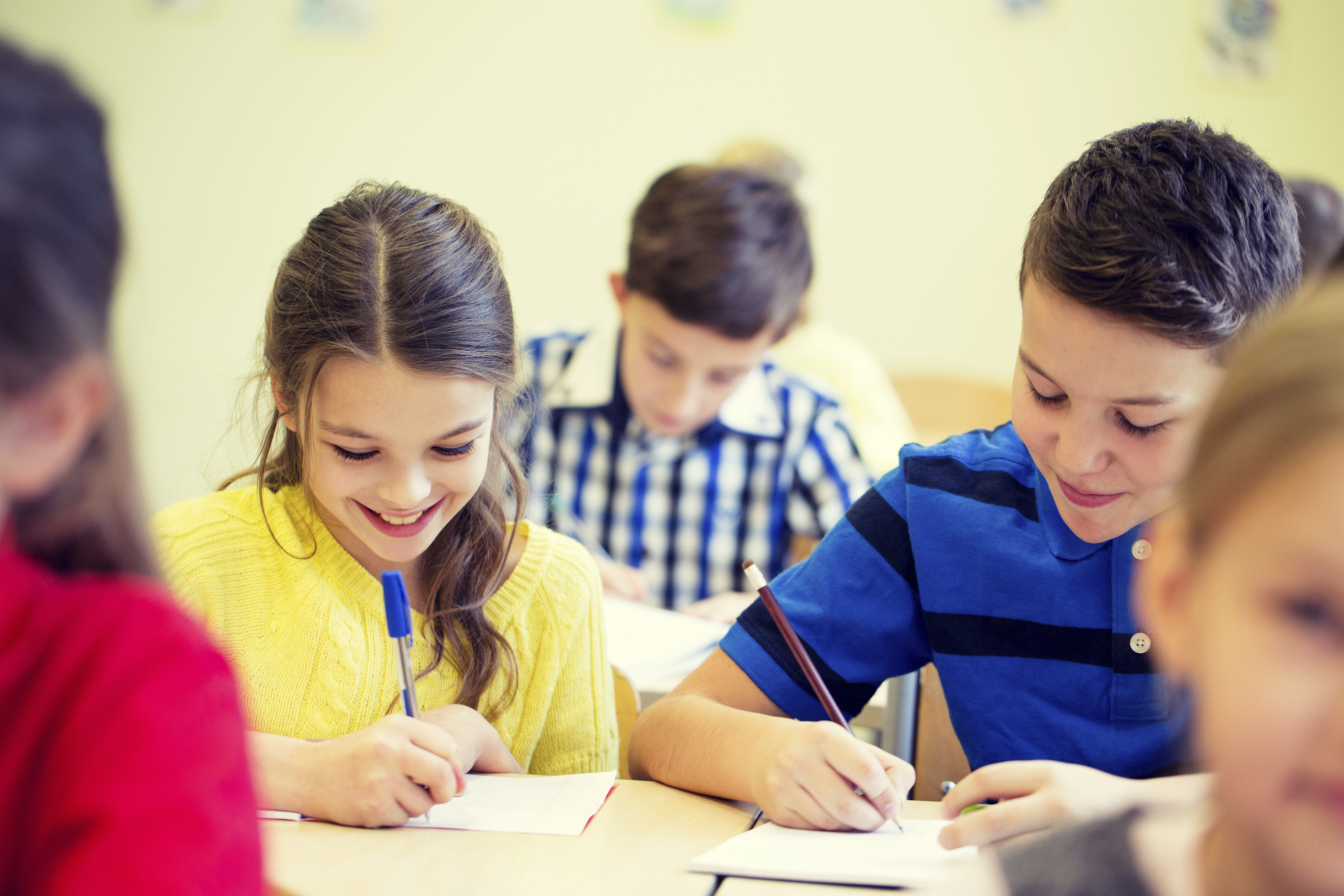 education, elementary school, learning and people concept - group of school kids with pens and notebooks writing test in classroom