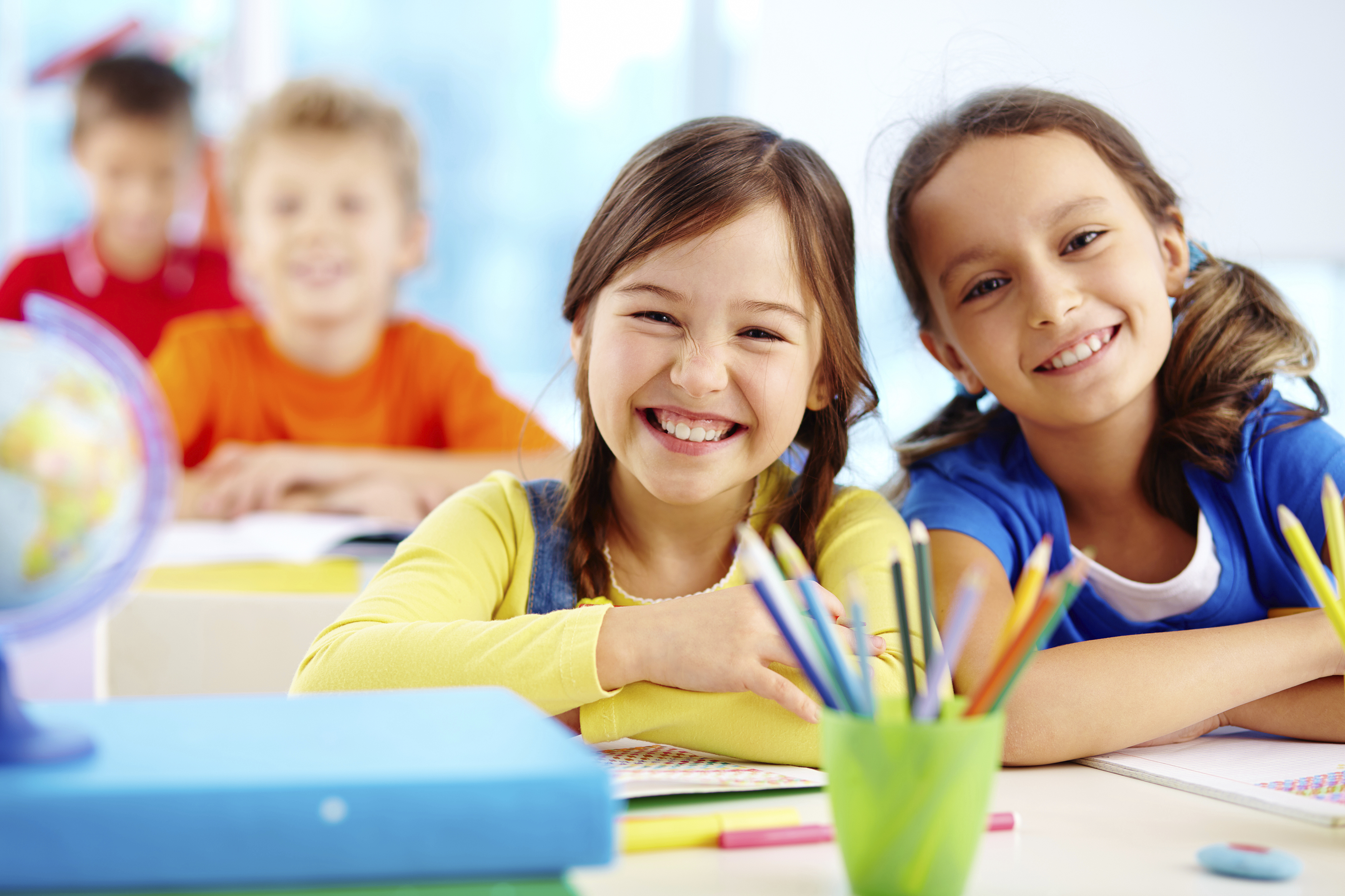 Portrait of two diligent girls looking at camera at workplace with schoolboys on background